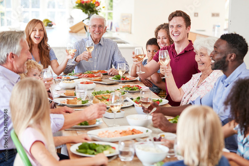 Group Of Multi-Generation Family And Friends Sitting Around Table And Making A Toast