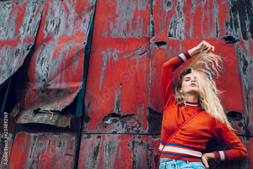 Lifestyle fashion portrait of young beautiful cute girl model. Odd bizarre strange unusual cute naughty blonde babe posing on old rusty metal gate background. Nice looking woman in trendy clothes.