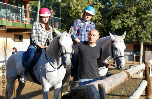 Positive mature couple with jockey learn to riding horse at farm