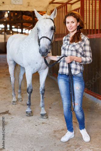 Female farmer standing with white horse at stabling indoor