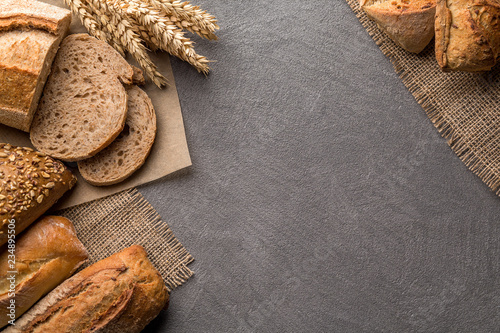 Bread background with wheat, aromatic crispbread with grains, copy space, top view. Brown and white whole grain loaves still life composition with wheat ears scattered around.