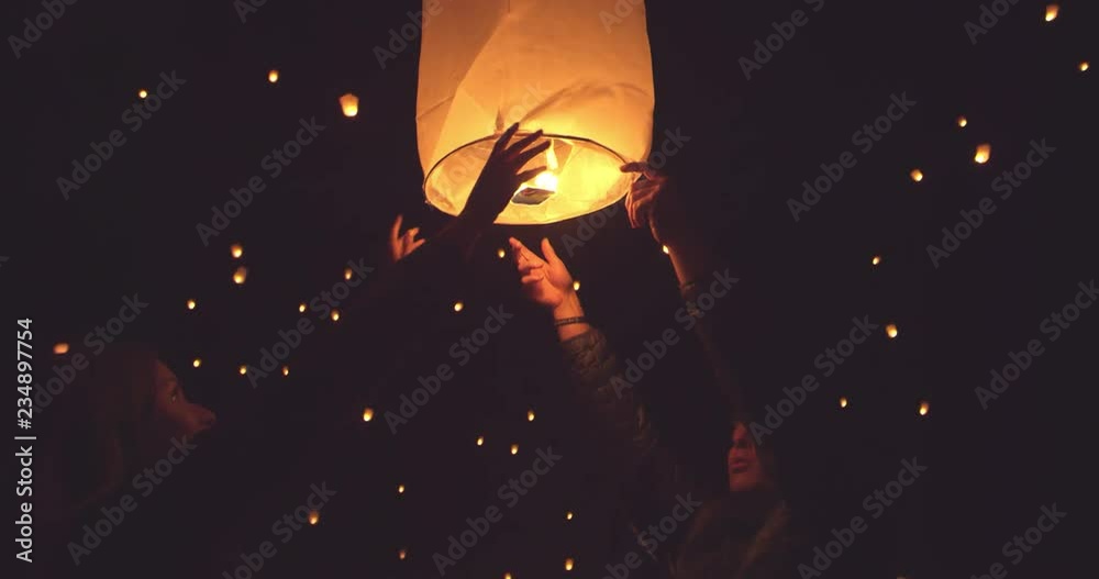 Happy young couple releasing flaming lantern at festival at night 