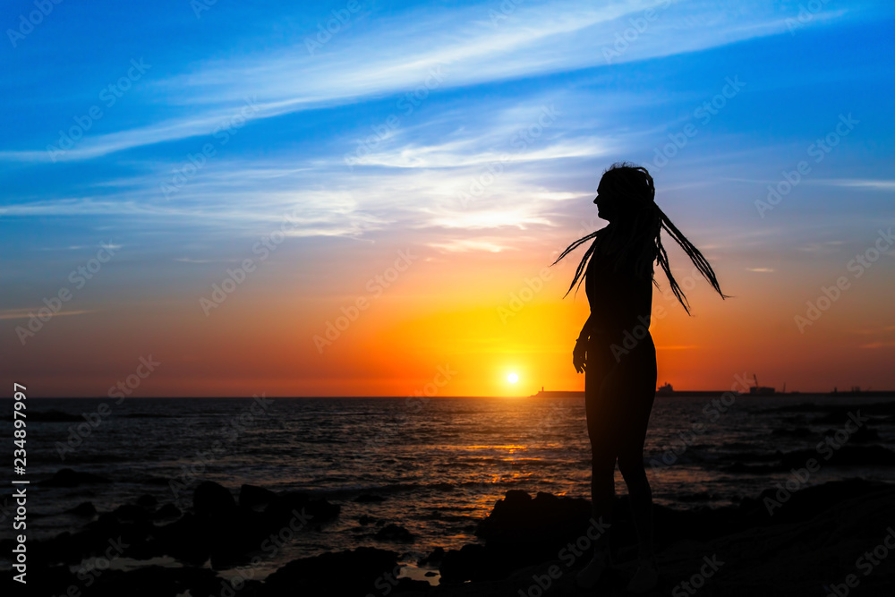 Silhouette of young woman on the sea coast during amazing sunset.