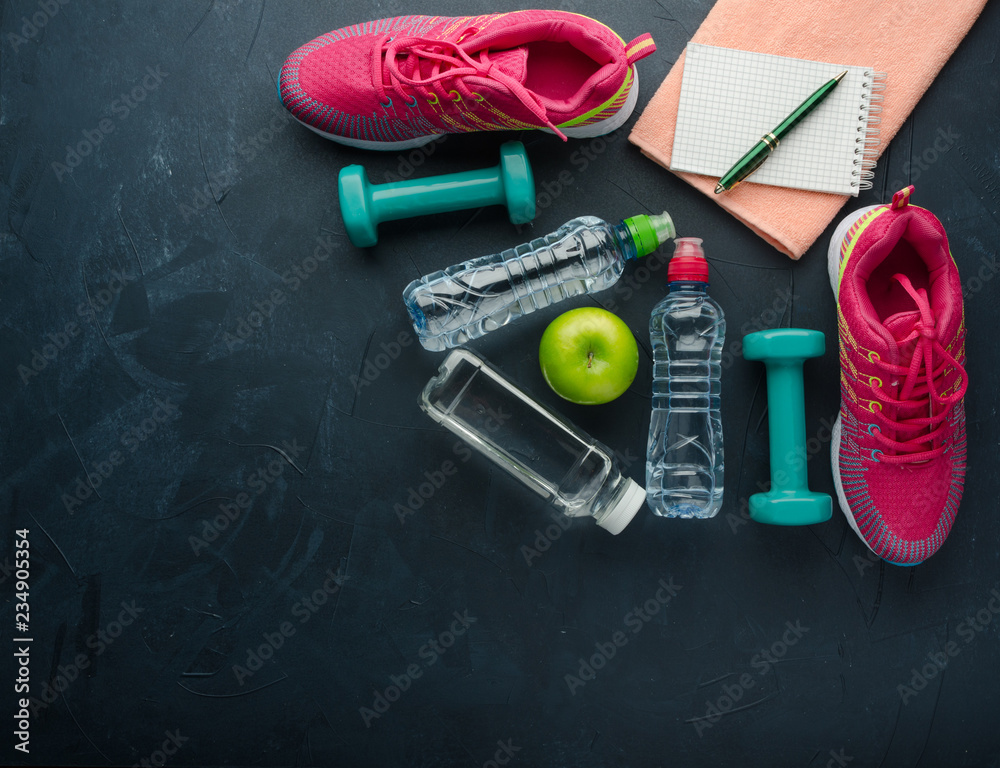 Sneakers dumbbells bottle of water and apple on black concrete Sneakers dumbbells bottle of water and apple on black concrete