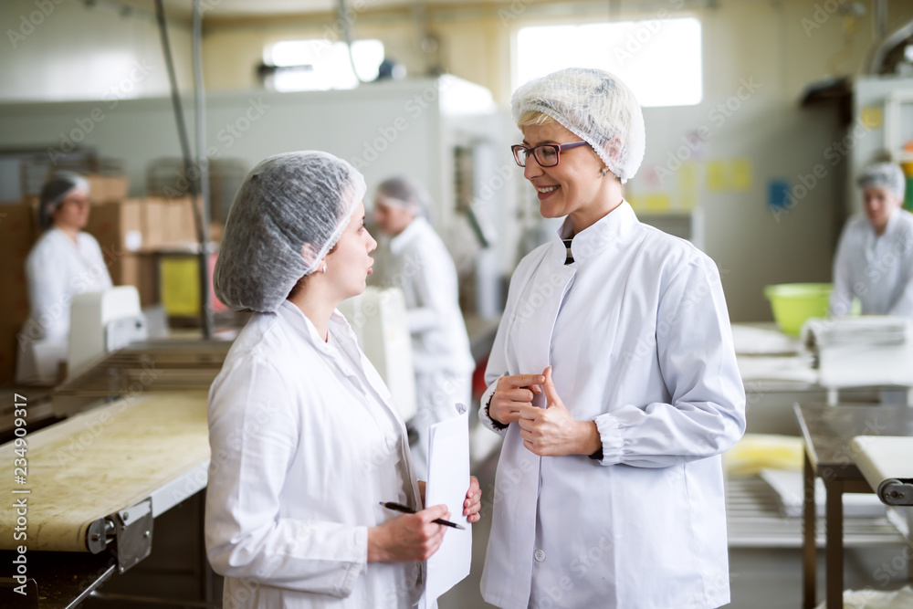 Obraz premium Two female workers discussing while standing in food factory.