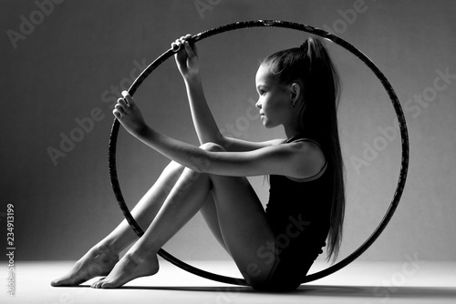 Portrait of a girl sitting inside a hoop for rhythmic gymnastics. Black background