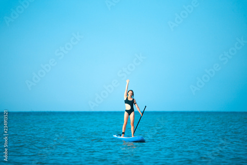Happy beautiful young girl with paddle board on a tropical beach. Blue sea in the background. Summer, vacation, sup paddleboarding or surfing, travel, lifestyle concept. © master1305
