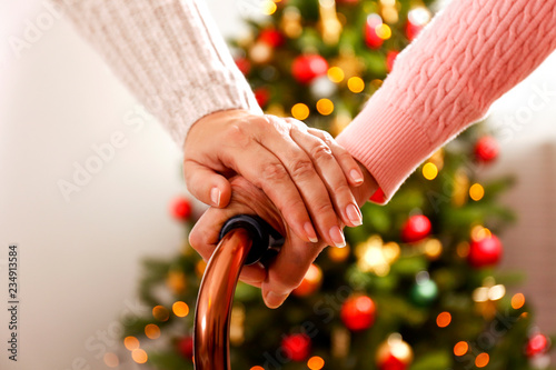 Elderly woman celebrating Christmas at home, with decorated holiday pine tree on background. Old lady at nursing home. Close up, copy space, cropped shot.