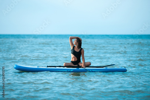 Happy beautiful young girl with paddle board on a tropical beach. Blue sea in the background. Summer, vacation, sup paddleboarding or surfing, travel, lifestyle concept.