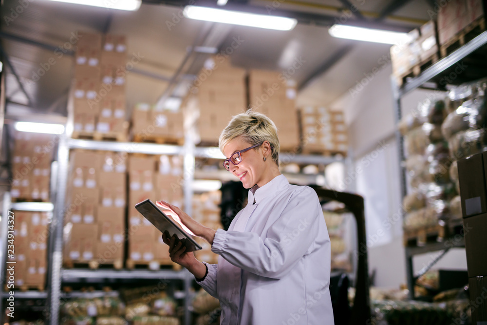 Happy Caucasian factory worker using tablet while standing in warehouse.