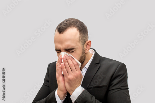 Young man sneez into white tissue. He keeps eyes closed. Young man is sick. Isolated on white background.