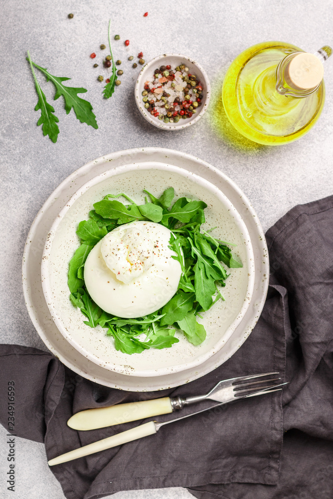 Delicious Creamy Italian Burrata Cheese Served with Olive Oil, fresh arugula and spices in a white plate Delicious Creamy Italian Burrata Cheese Served with Olive Oil, fresh arugula and spices in a white plate