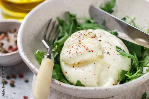 Delicious Creamy Italian Burrata Cheese Served with Olive Oil, fresh arugula and spices in a white plate