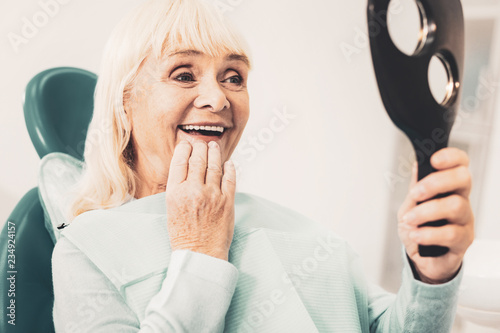Mature woman with mirror looking at her denture photo