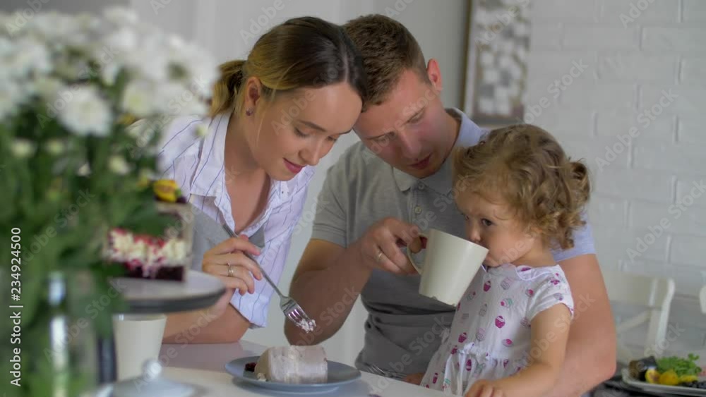 Happy family have breakfast. Mom dad and daughter drink tea and eat cake Happy family have breakfast. Mom dad and daughter drink tea and eat cake