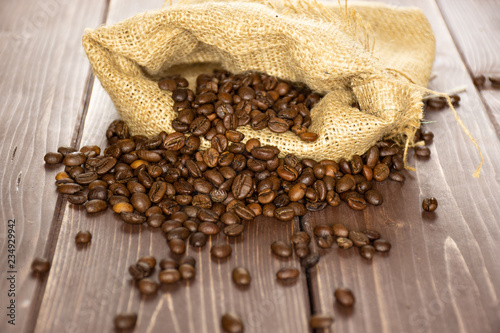 Lot of whole dark brown coffee beans sweet arabica variety in a jute bag on brown wood