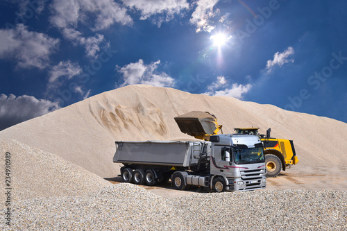 Wheel loader loads a truck with sand in a gravel pit photo