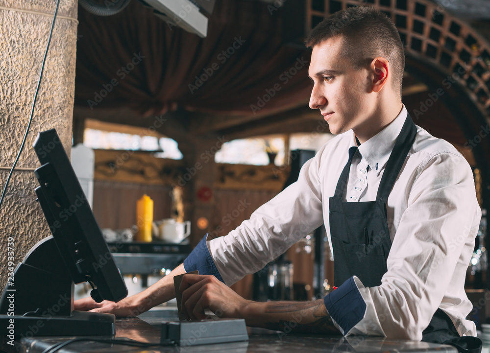 small business, people and service concept - happy man or waiter in apron at counter with cashbox working at bar or coffee shop small business, people and service concept - happy man or waiter in apron at counter with cashbox working at bar or coffee shop