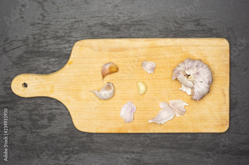Peeling garlic bulb. recipe step by step farfalle with arugula leaves on chopping board flatlay on grey stone