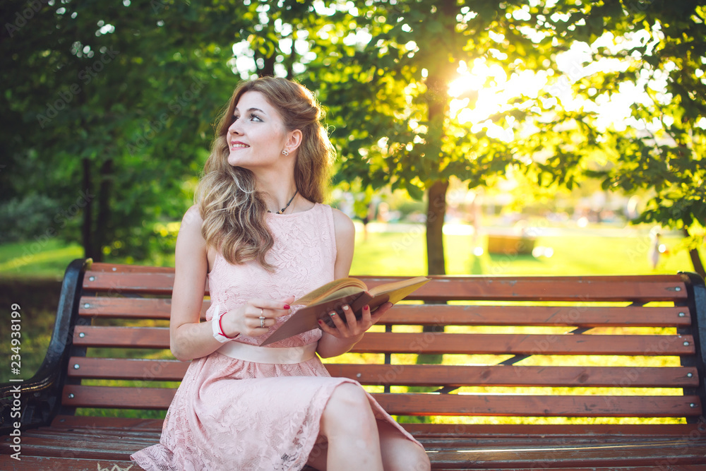 A young girl reading a book sitting on a bench at sunset. A young girl reading a book sitting on a bench at sunset.
