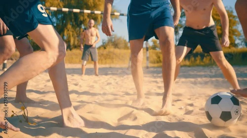 Soccer players in dynamic action funny play on the sand in beach football in summer sunny day under sunlight.
