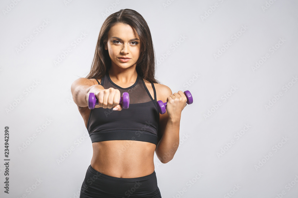 Enjoy your body! Beautiful young woman doing exercises with dumbbells at biceps. Photo athletic woman with perfect body isolated on white background. Strength and motivation, close-up. Enjoy your body! Beautiful young woman doing exercises with dumbbells at biceps. Photo athletic woman with perfect body isolated on white background. Strength and motivation, close-up.