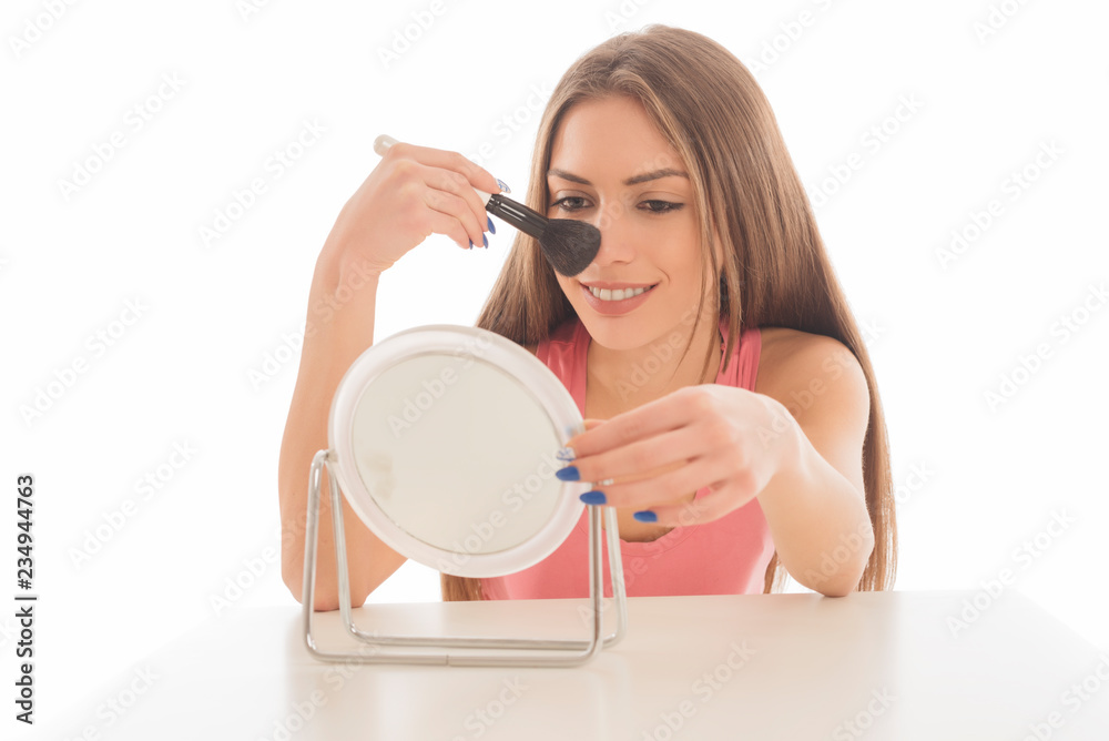 Beautiful young woman applying make up with a brush on white background Beautiful young woman applying make up with a brush on white background