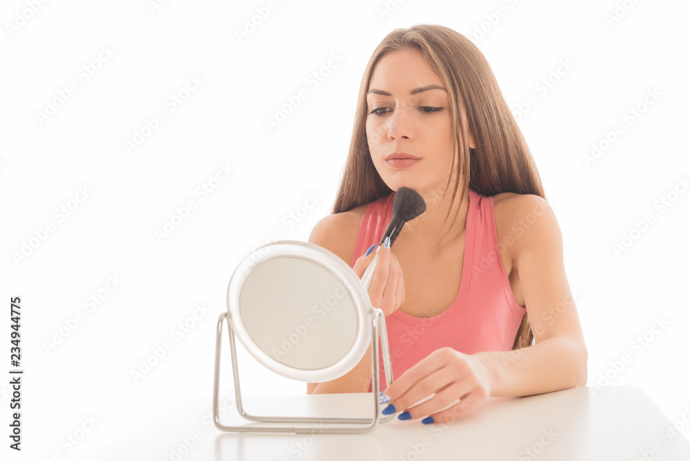 Beautiful young woman applying make up with a brush on white background Beautiful young woman applying make up with a brush on white background
