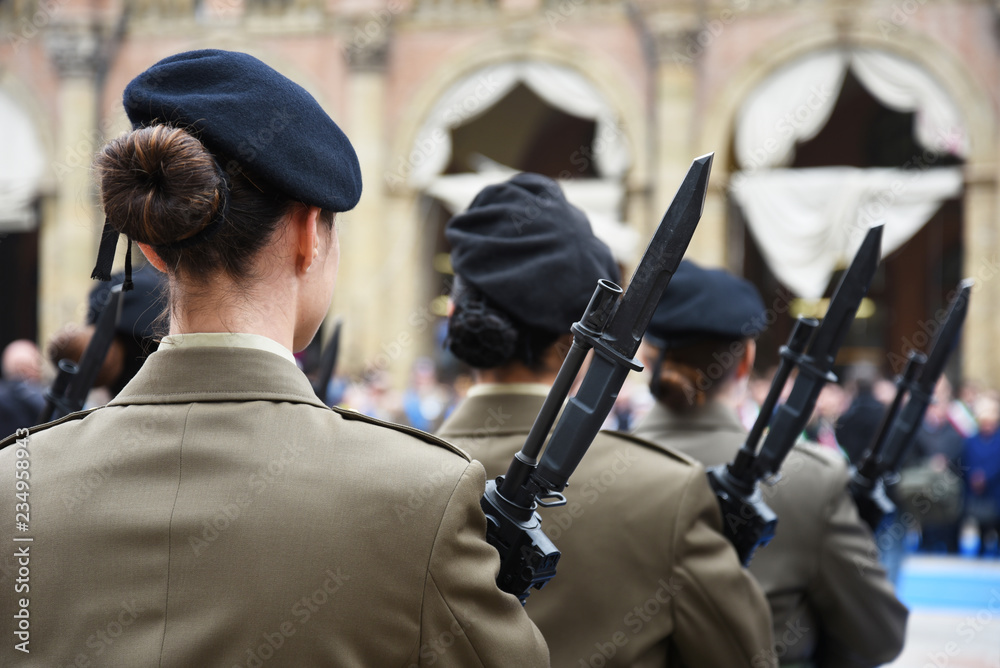 Detail with uniformed women standing during the military ceremony in Bologna, Italy. In the foreground, a woman seen from behind with a bayonet rifle.