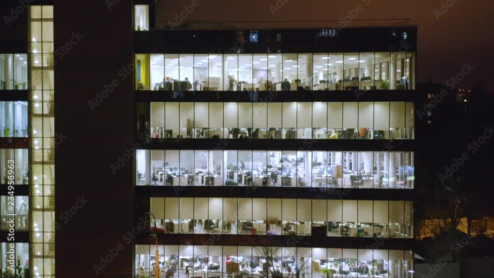 Aerial look-down view of the modern office building with glowing windows with office people inside Aerial look-down view of the modern office building with glowing windows with office people inside