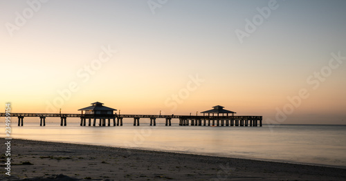 Fort myers beach pier before sunrise with flat water and yellow orange sky