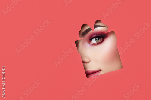 Face of a Young Beautiful Woman with a Beauty Make-up. Extension Eyelashes, Beautiful Green Eyes with Pink Shadows. Gift Box. Christmas Patterns. Red Paper