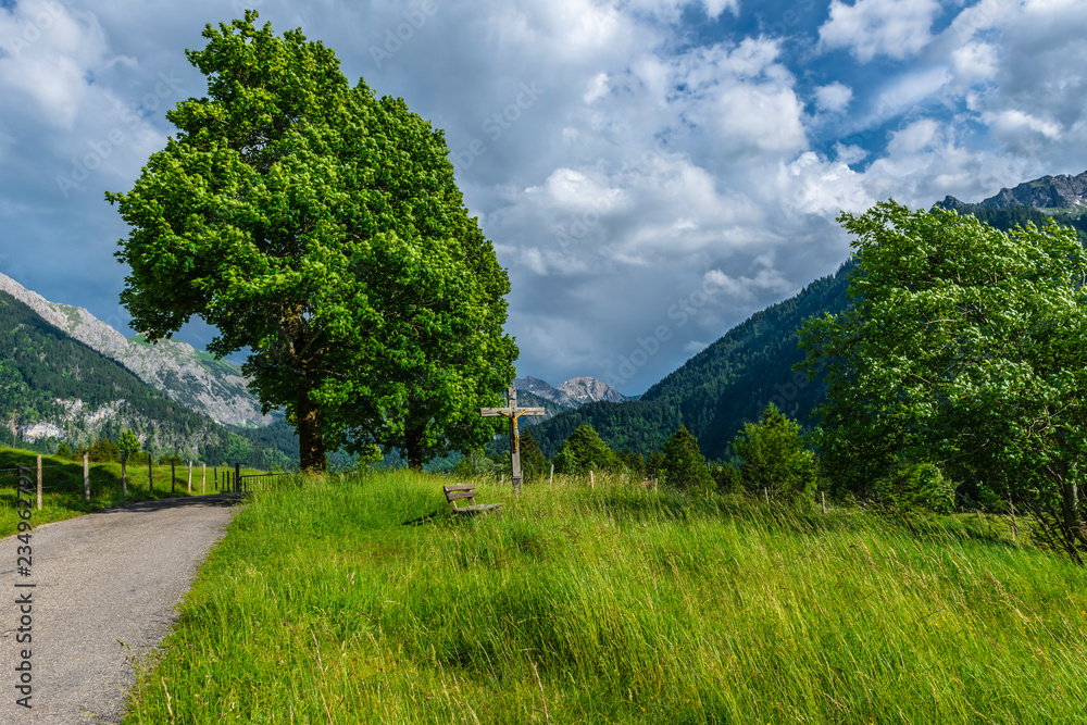 Wegkreuz und Bank unter einem Baum strümisches Wetter in den Alpen