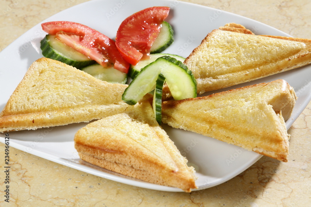 A shot of three triangle sandwiches with tomatoe and cucumber on the side A shot of three triangle sandwiches with tomatoe and cucumber on the side