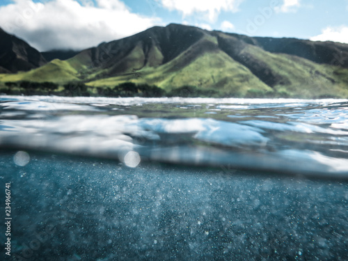 Cool Split Photo Half Underwater with Clear Blue Ocean Water Drops and Lush Green Mountain Background with Sunshine on Clear Beautiful Day in Tropical Island Paradise on Maui Hawaii