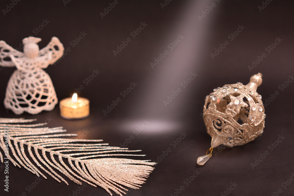 Obraz premium Christmas decoration on black background. White angel, candle, silver feather and christmas tree bauble. Light ray on copy space