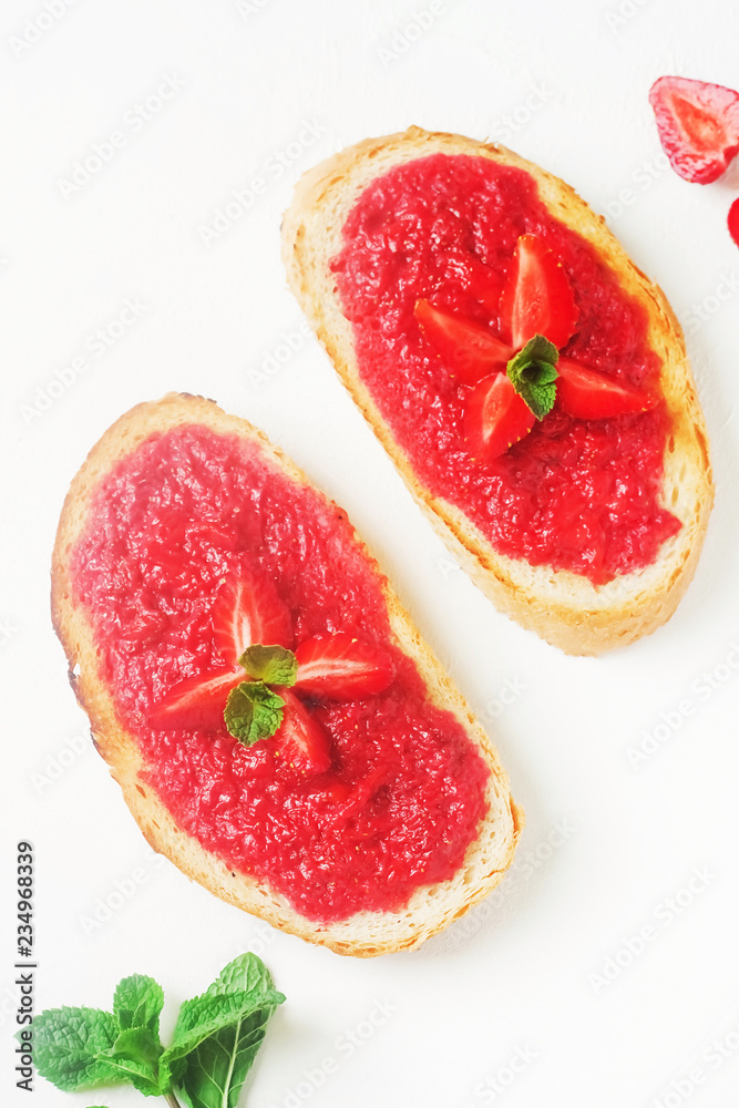 Slices of french bread with strawberry jam and mint on white background - healthy summer breakfest Slices of french bread with strawberry jam and mint on white background - healthy summer breakfest