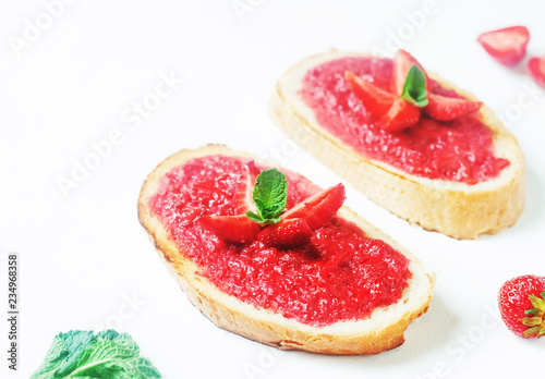 Slices of french bread with strawberry jam and mint on white background - healthy summer breakfest