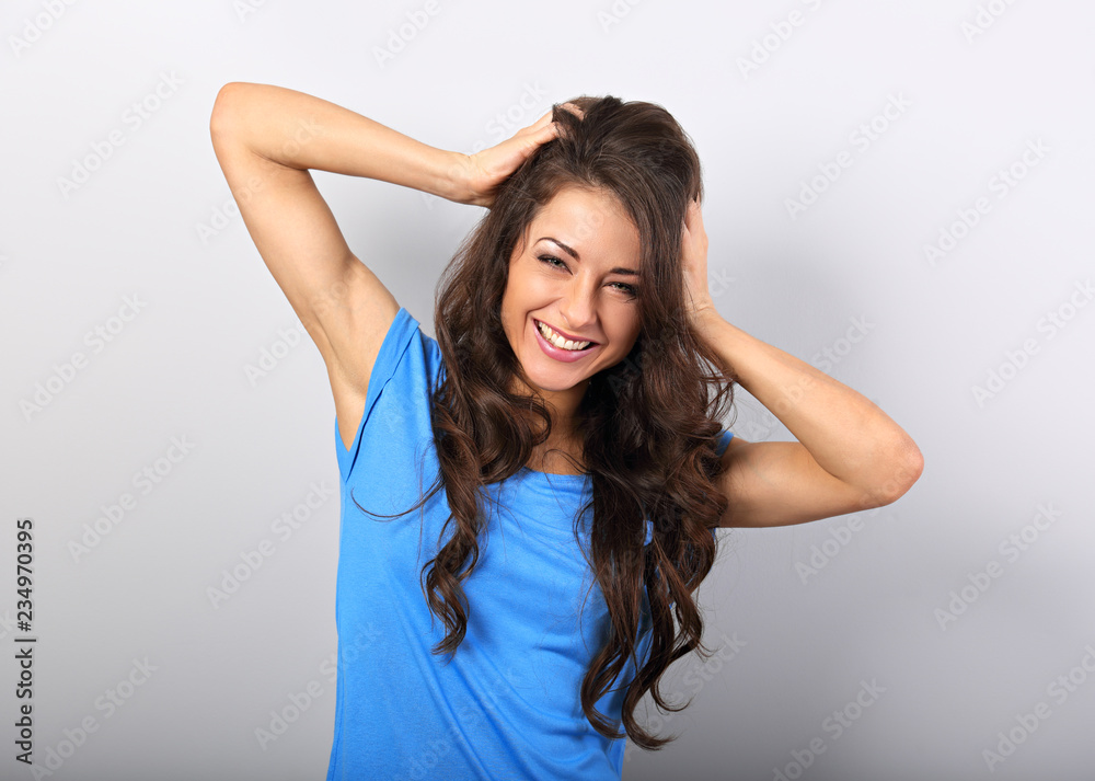 Beautiful excited laughing woman holding the head the hands in blue shirt with long curly hairstyle. Closeup portrait with empty copy space. Beautiful excited laughing woman holding the head the hands in blue shirt with long curly hairstyle. Closeup portrait with empty copy space.