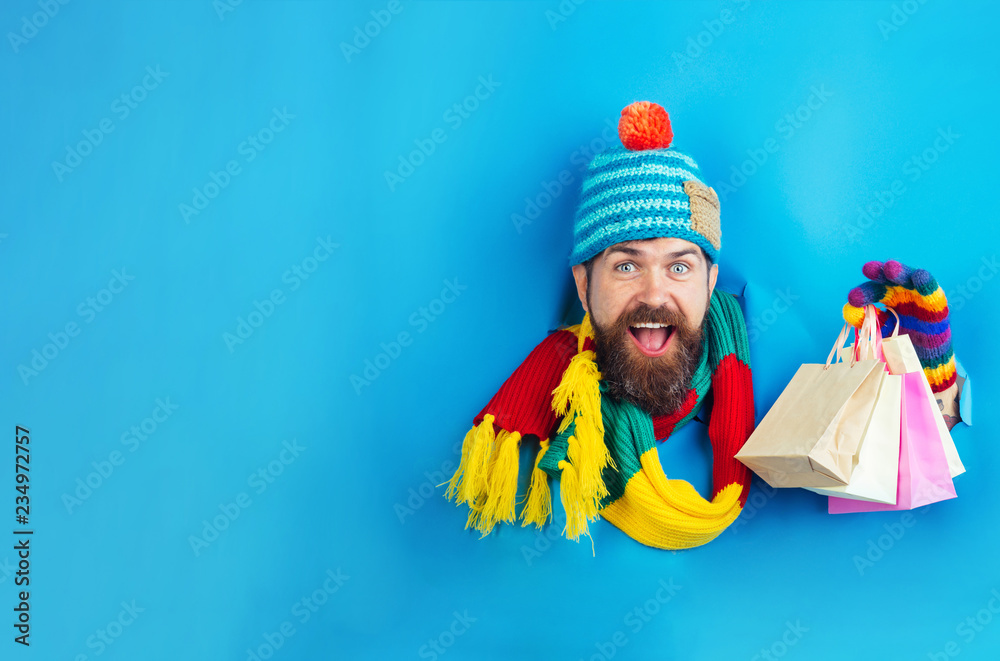 Gift and present. Bearded man in warm clothes holds shopping bags. Sale, discount, fashion, retail, consumer, advertisement, black friday concept. Man with shopping bags looking through hole on paper.