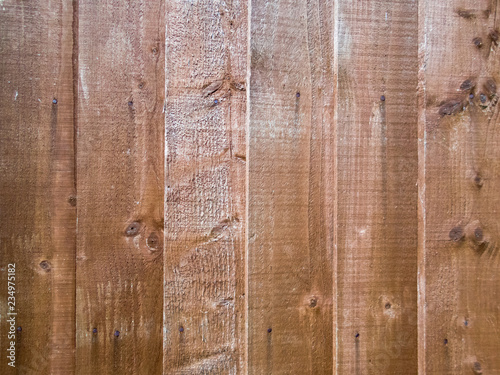 Close-up of a brown wooden featherboard or closeboard fence with knotted planks. Rustic textured background or flat lay concept.