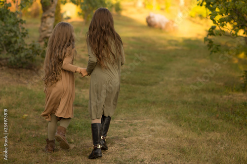 two girls, teenagers, go on the green grass, embracing. back view.