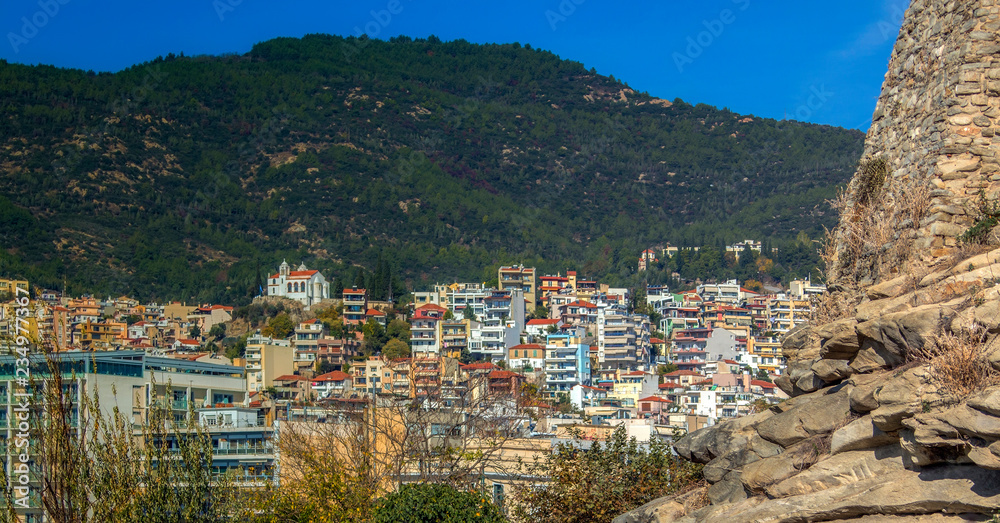 Landscape of Kavala. Through the rock of the fortress wall to the harbor and the buildings under the green hills of the mountain. Aegean Sea, Greece.