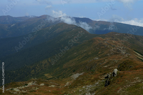 The peaks of the Carpathian Mountains. Mountain ranges covered with forests under blue clouds