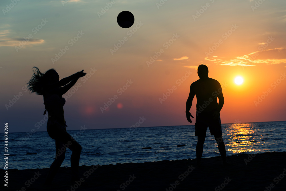 Silhouette of two friends playing beach Volleyball on the beach in sunset