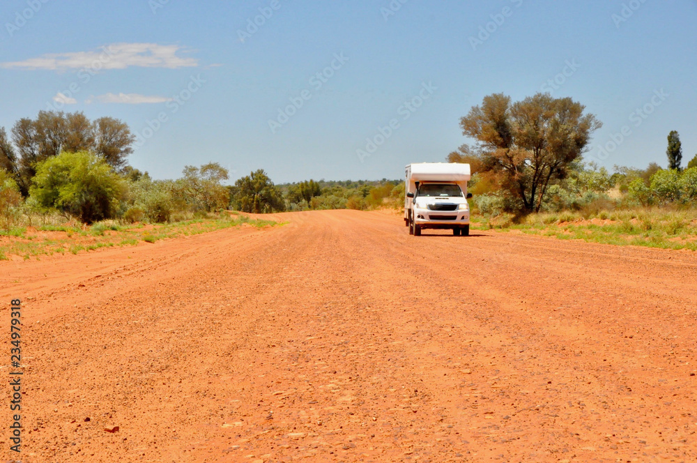 front view of a white camper van on the red gravel road in the australian outback in alice springs on a sunny day with blue sky