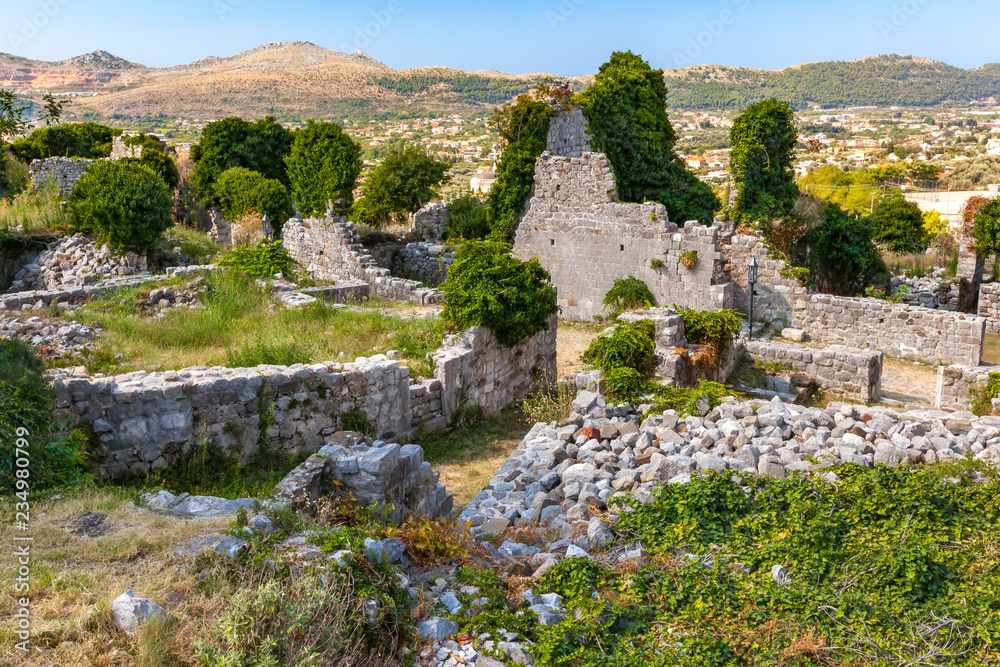 The inner courtyard of the ancient city with dilapidated walls, the land overgrown with green grass with trodden paths, view from above. Summer landscape in Fortress Old Bar Town, Montenegro.