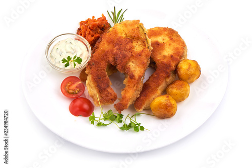 Crispy breaded fish fillet with herbs, sauce and potatoes, isolated on a white background. Close-up