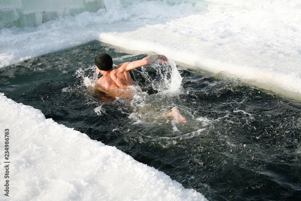 Man is swimming outdoors in the ice hole in the lake in the winter. Man dippes in a ice hole. - obrazy, fototapety, plakaty 