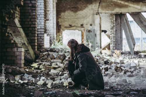 Sad man kneels and looks at ruins post apocalypse on earth, fallen bricks background.